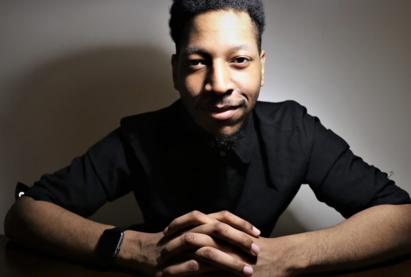 A man posing with hands folded in a black shirt