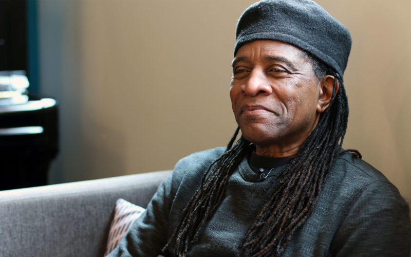 A man sitting with a black shirt and black cap on a couch