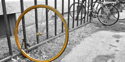A group of bicycles chained to a rack one of which is just one tire, presumably because the rest of the bike was stolen.