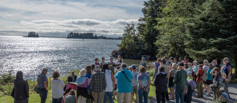 An audience gathers in front of a lake