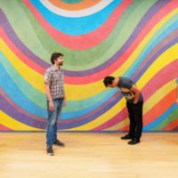 4 caucasian men posing in front of a rainbow swirled background