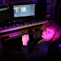 A Caucasian woman sitting with pink lights against her skin, with a keyboard and computer in the background