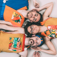 3 people in colorful clothes laying on the ground, looking up at the camera