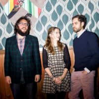 A colorful photo of two Caucasian men and one Caucasian woman posing nonchalantly