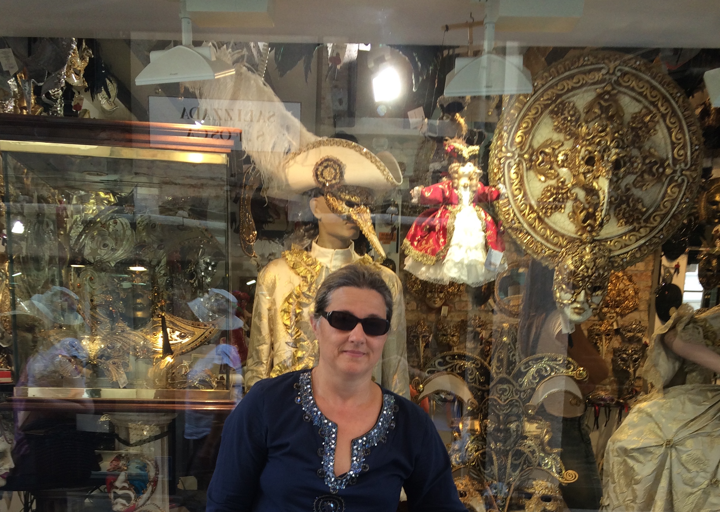 Ljiljana Becker/Jovanović wearing sunglasses standing outside a store front display featuring gold-laminated masks.