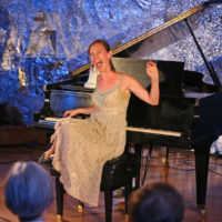 A singer sitting on a piano bench performing