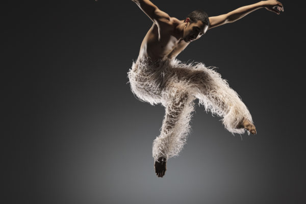A dancer wearing feathered pants jumps
